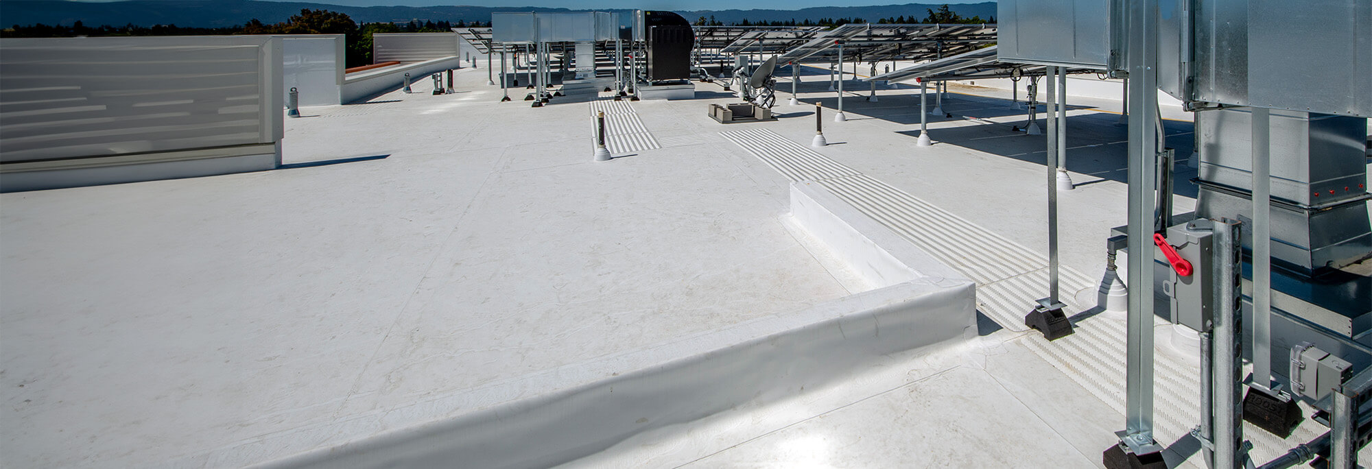 Wide view of a white commercial flat roof with solar racking and mechanical equipment