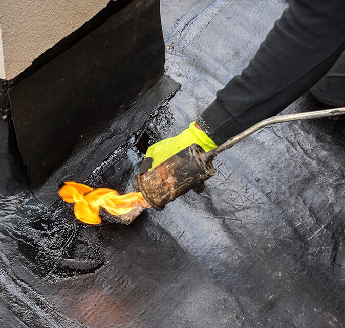 Close-up of a gloved hand torch-applying a modified bitumen roofing membrane