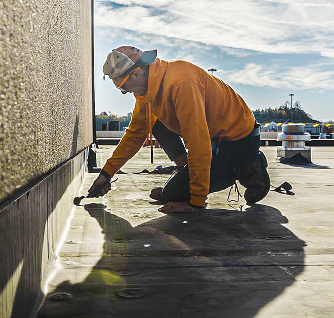 Roofer sealing a flat roof edge and wall flashing with a hand tool