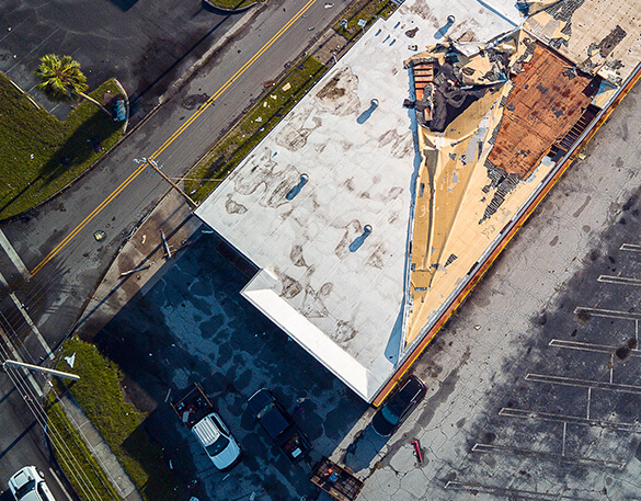Aerial view of a commercial roof with a section of membrane torn away exposing the decking