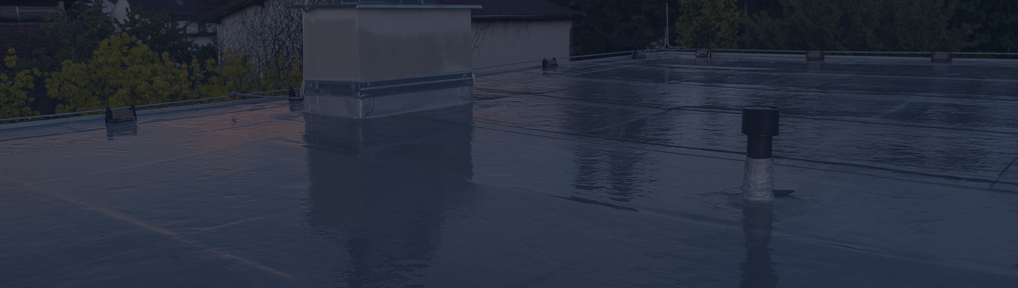 Wet commercial flat roof at dusk showing a roof curb and vent stack