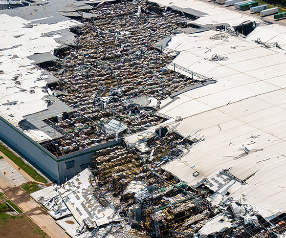 Aerial view of a large warehouse roof torn apart by severe storm damage